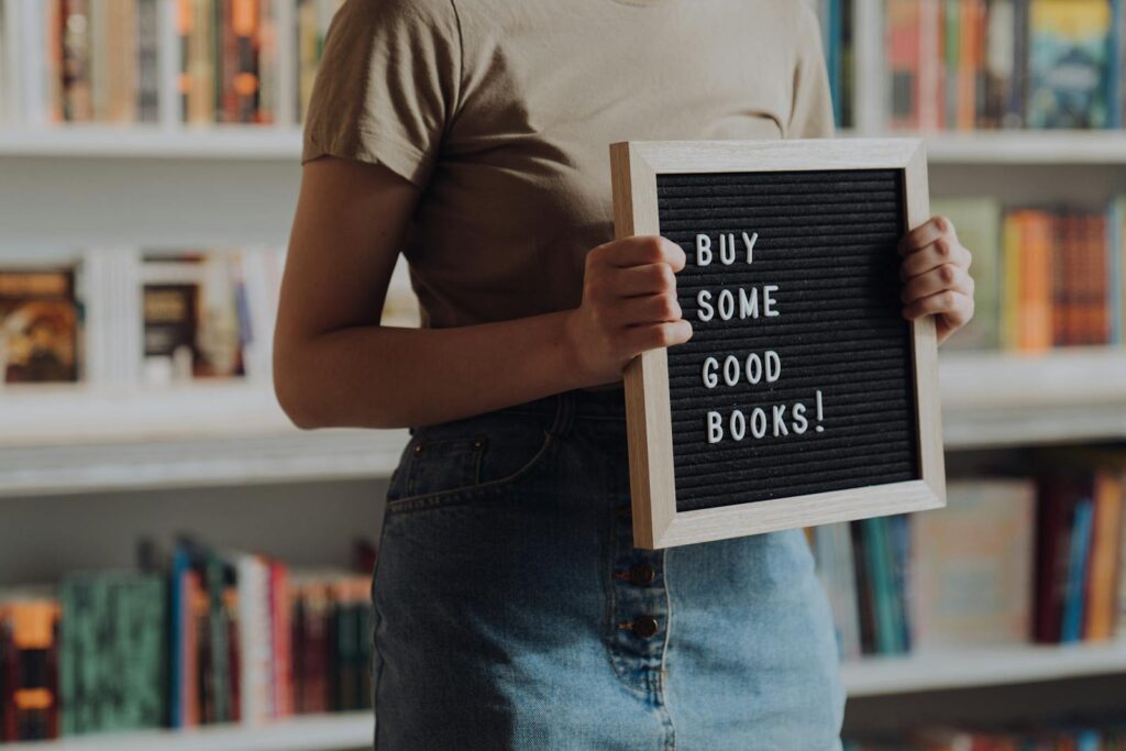 Man in Brown Crew Neck T-shirt and Blue Denim Jeans Holding Black and White Book