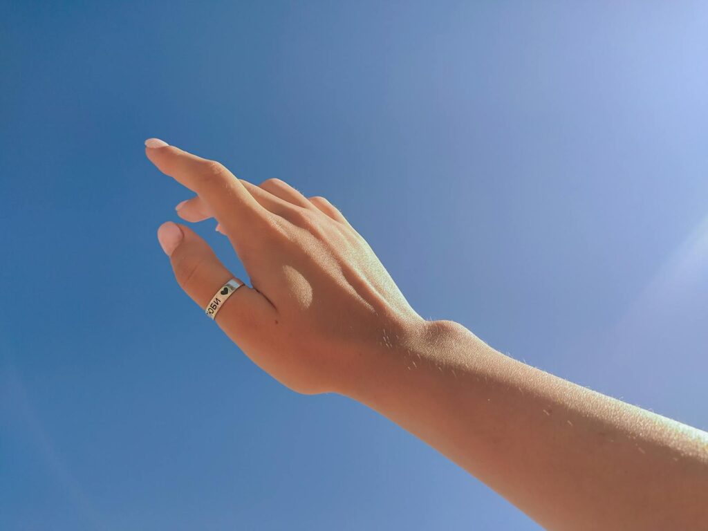 From below crop unrecognizable female hand with ring on thumb outstretched against cloudless blue sky on sunny day