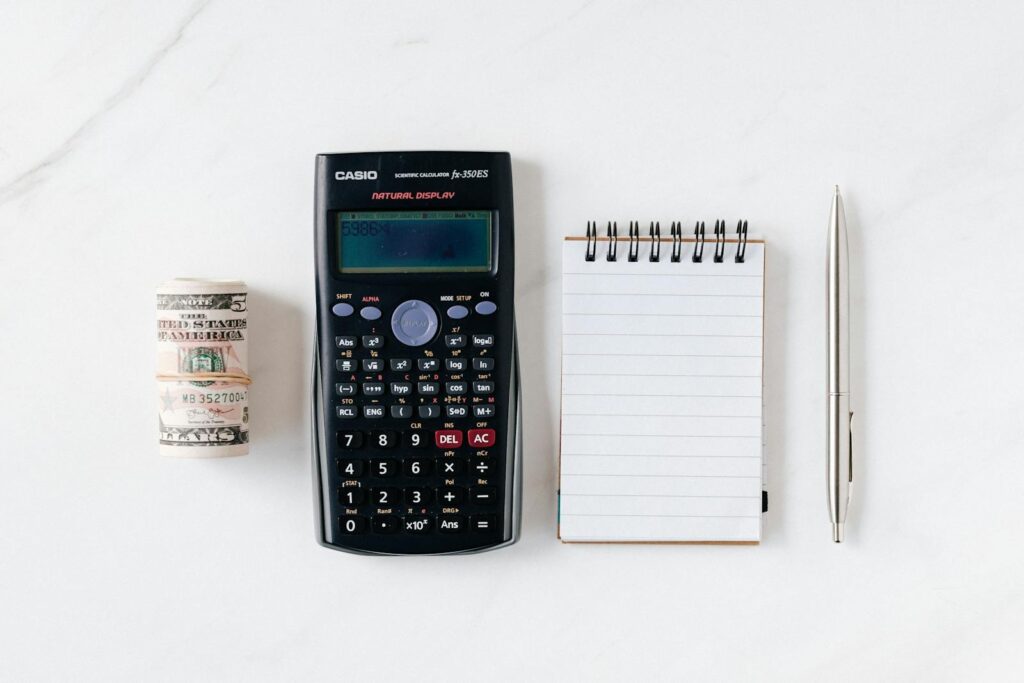 Top view of financial tools including a calculator, notepad, pen, and rolled cash on a white background.