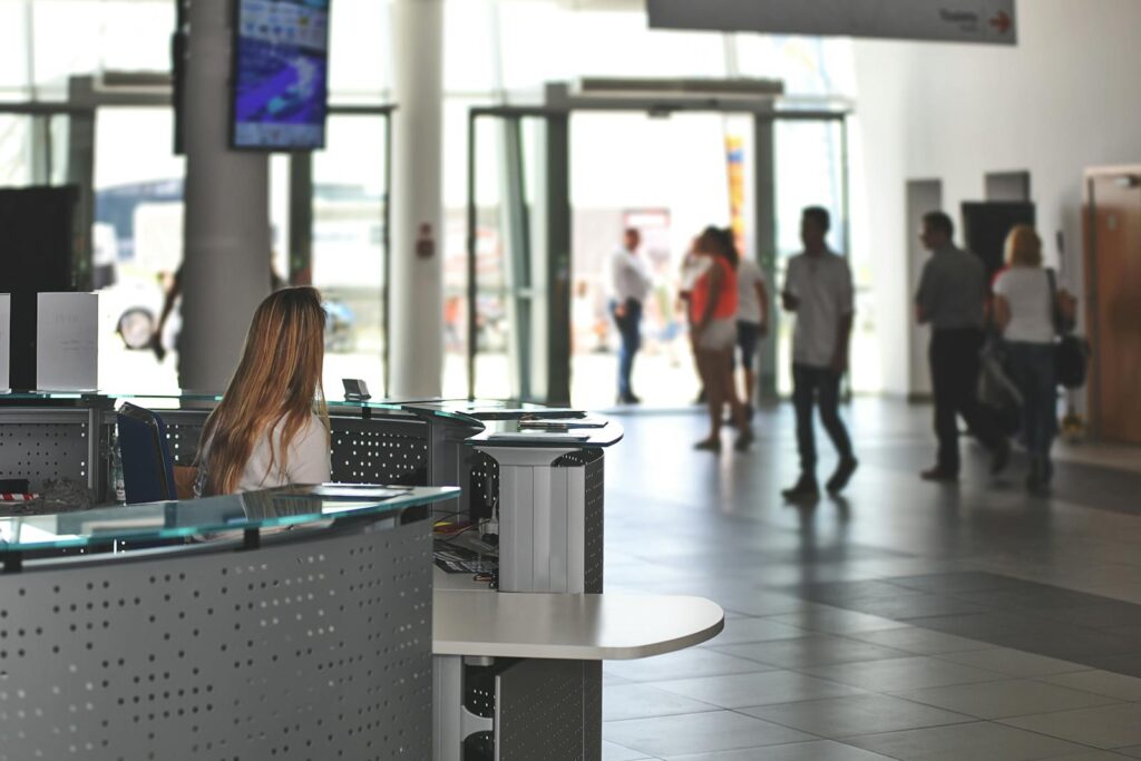 A bustling office reception area with people walking and a receptionist at a modern desk.