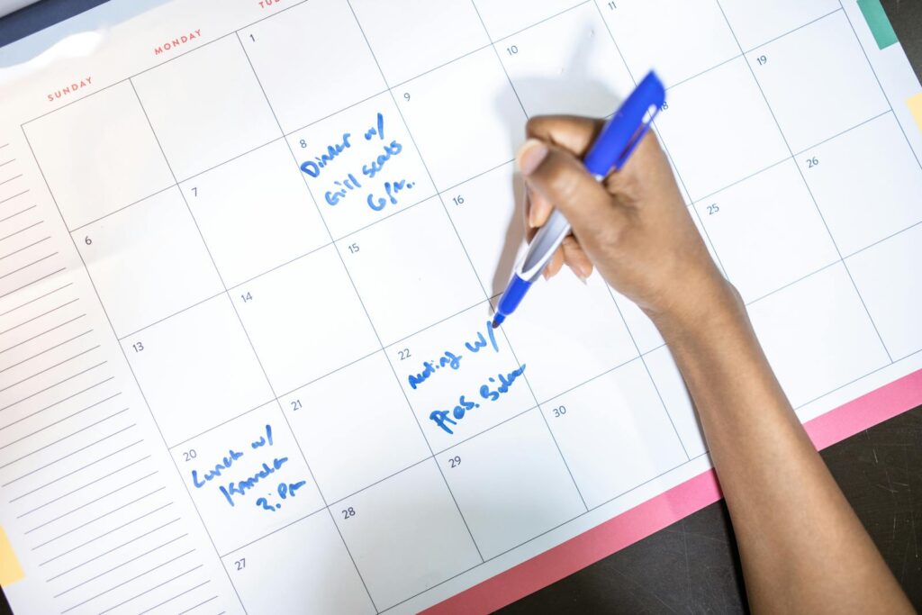 Person writing appointments on a calendar with a blue pen. High angle view.