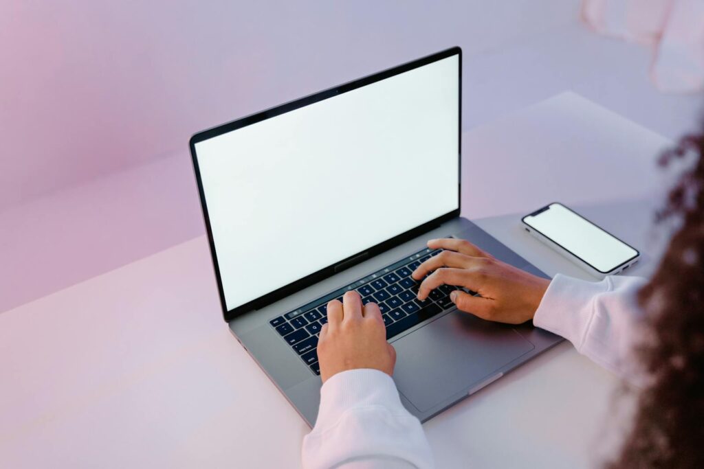 Person in White Long Sleeve Shirt Using Laptop Beside Mobile Phone